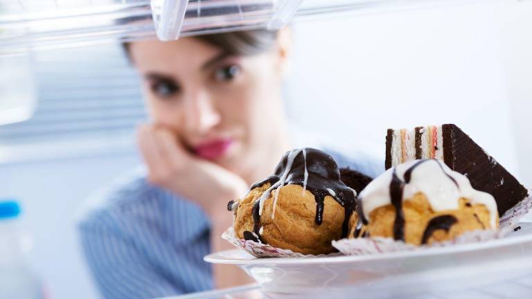 Mujer asomándose al refrigerador donde hay postres.