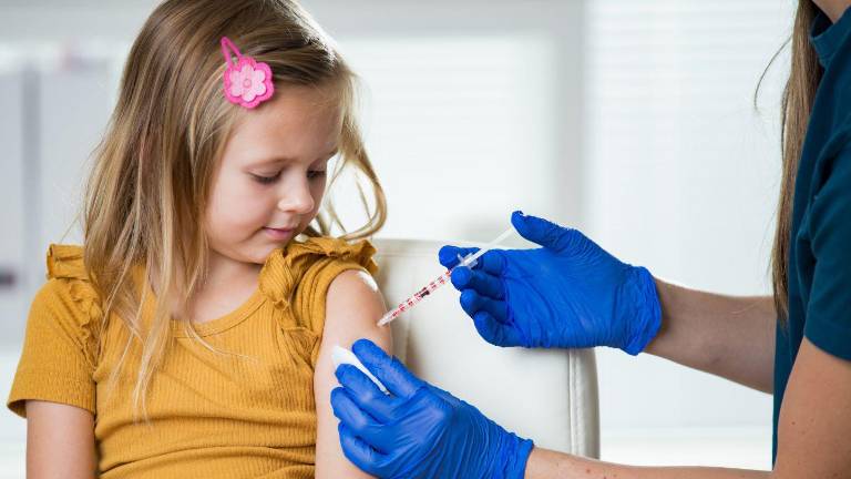 Niña recibiendo dosis de vacuna por una profesional de la salud.