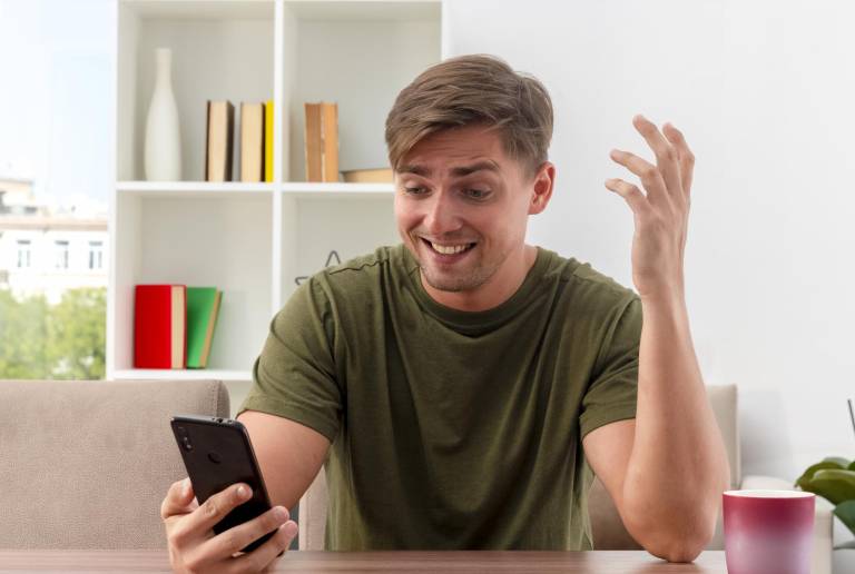 $!Un hombre viendo su celular con emoción.