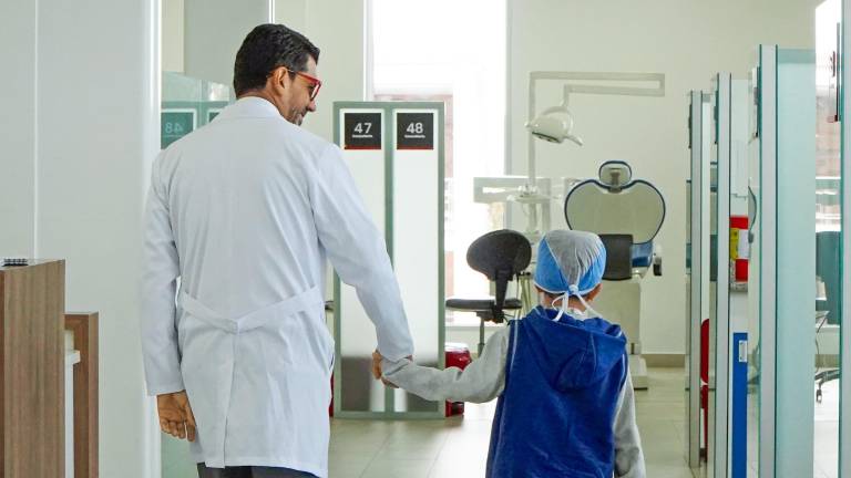 Un niño camina tomado de la mano de un doctor.