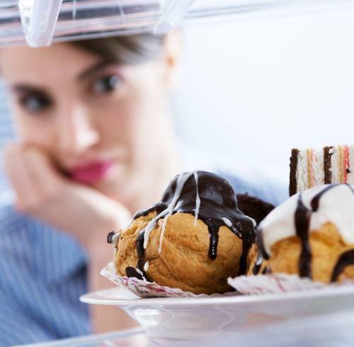 Mujer asomándose al refrigerador donde hay postres.