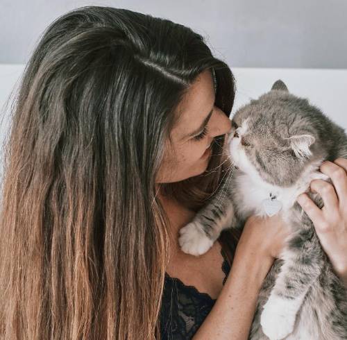 Una mujer dándole un beso y abrazo a su gato.