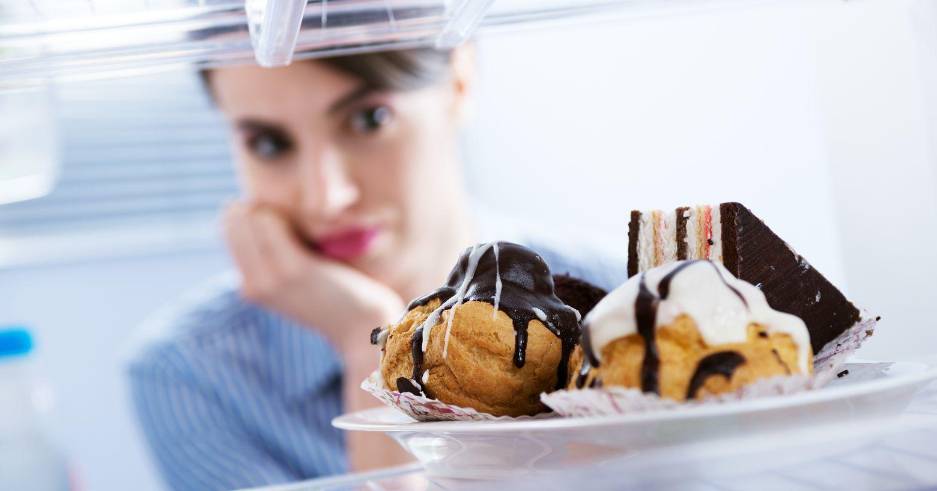 Mujer asomándose al refrigerador donde hay postres.