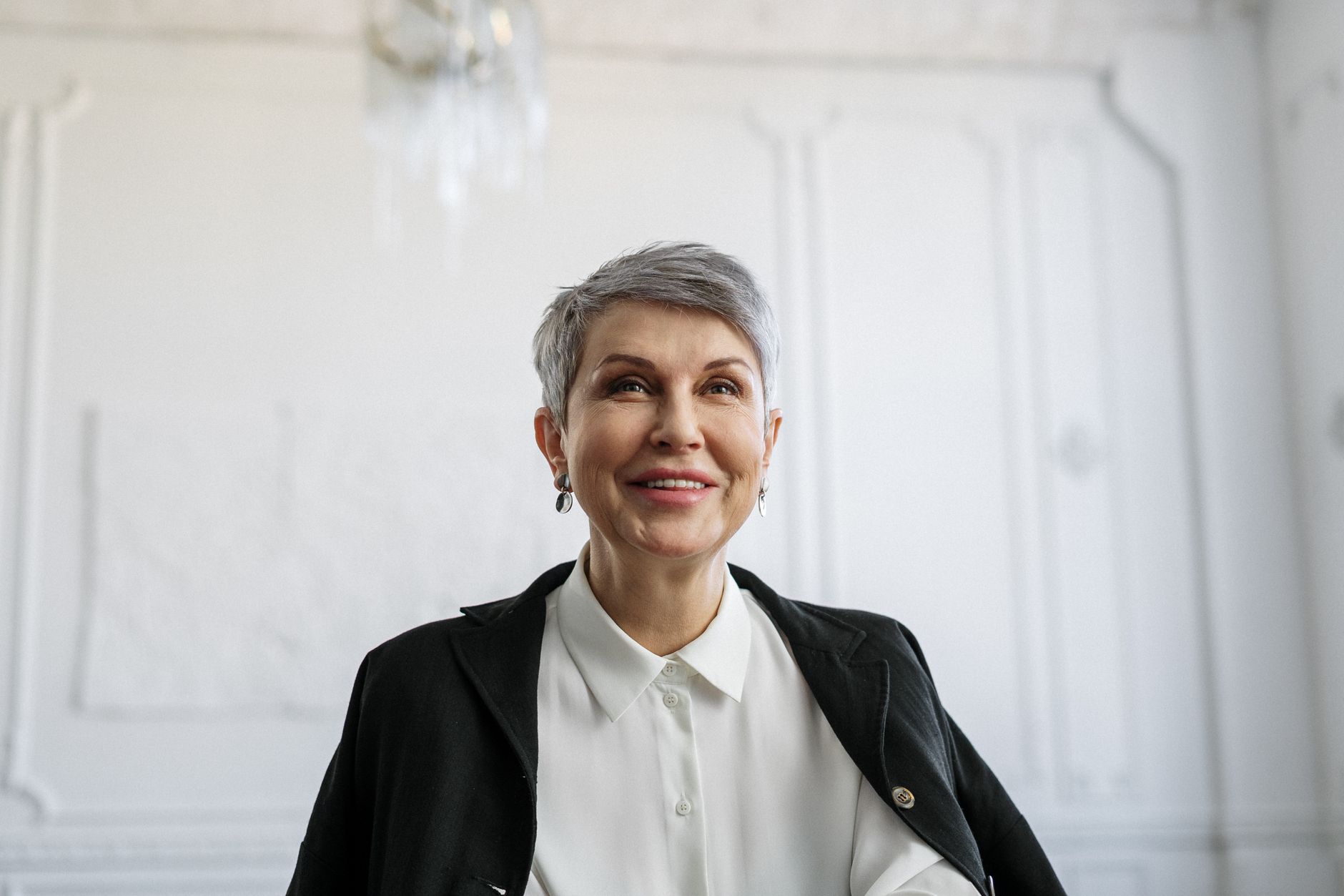 Mulher idosa sorridente vestindo traje formal, aparentando confiança em um ambiente interno.