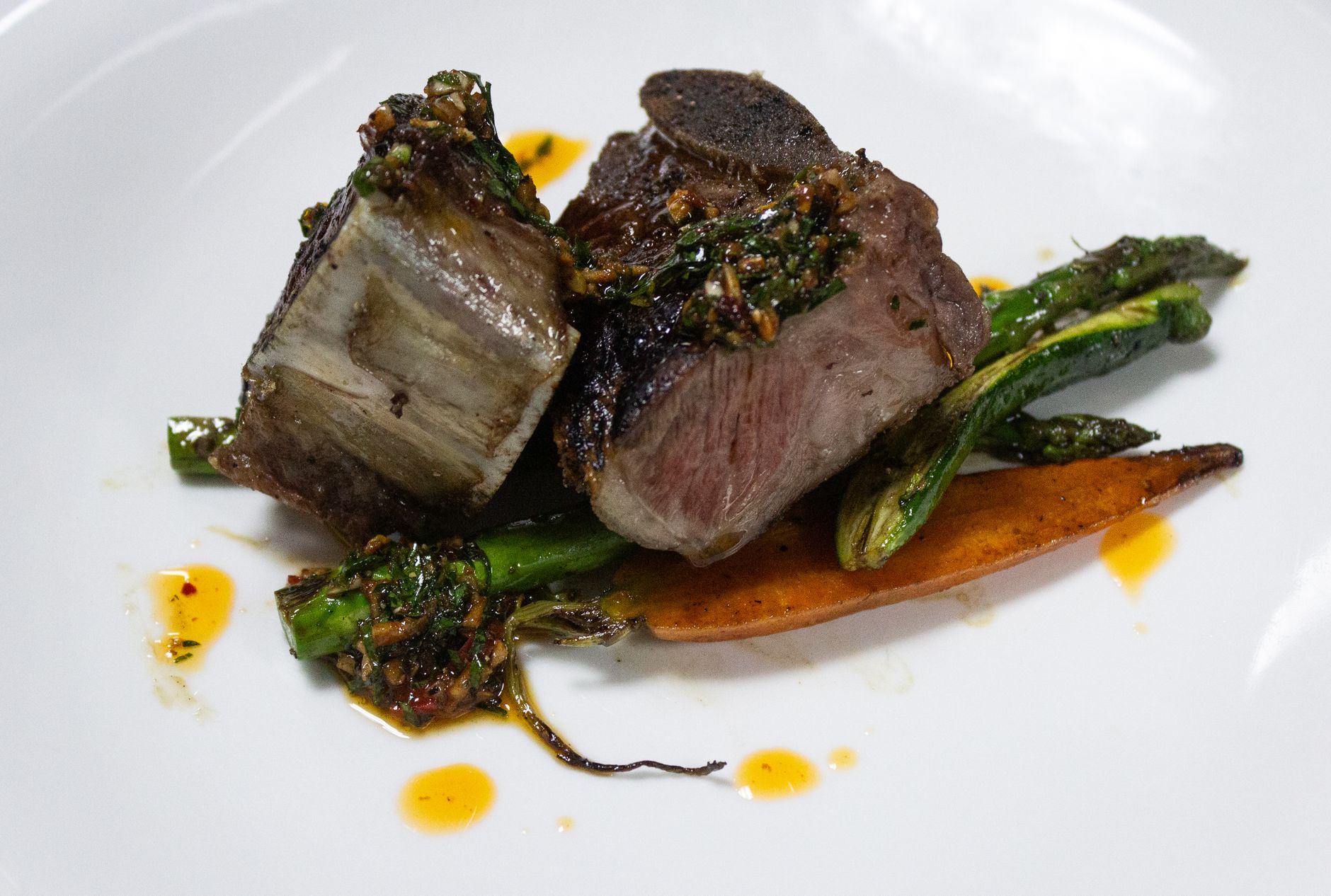 Close-up de um prato de bife gourmet com aspargos e cenouras, exibindo arte culinária.