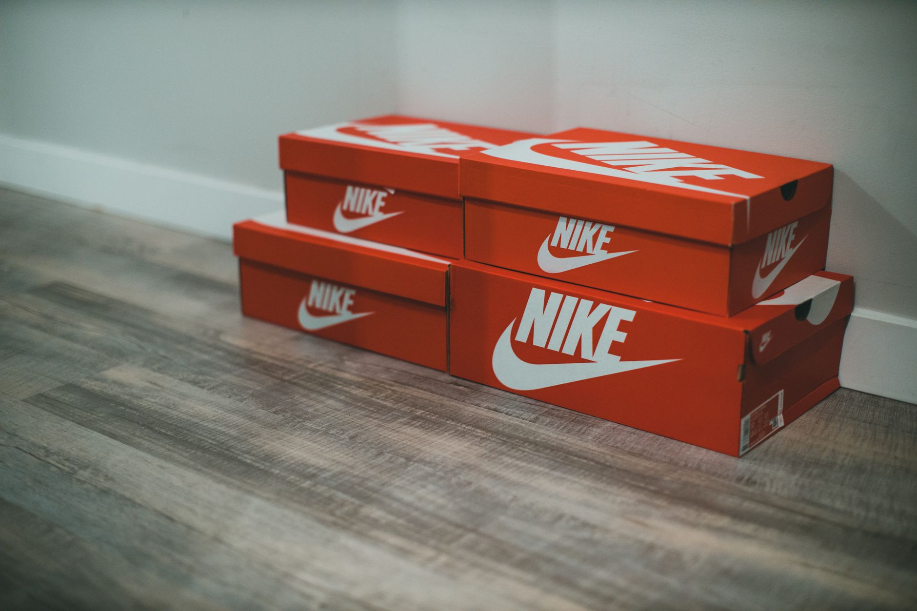 Caixas de tênis Nike vermelhas empilhadas ordenadamente em um chão de madeira interno.