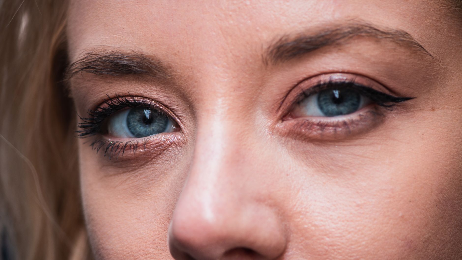 Detalhe em close-up dos olhos azuis de uma mulher, destacando a maquiagem natural e o delineador.