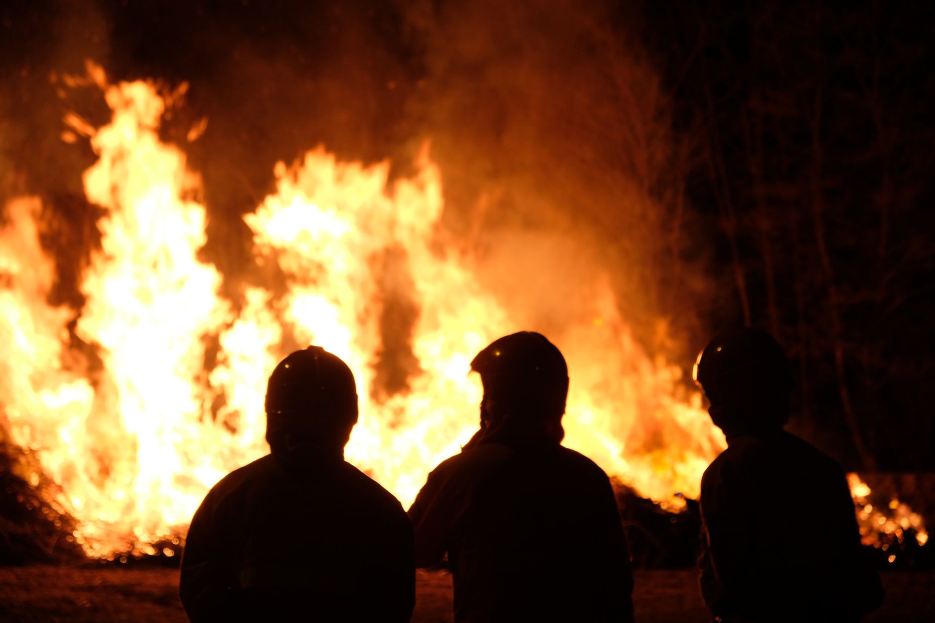 Silhueta de três bombeiros observando e gerenciando um grande incêndio florestal à noite.